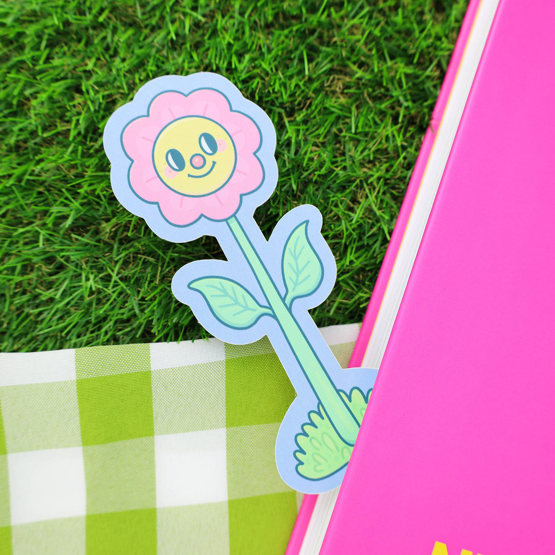 Flower-shaped bookmark with a face on a grassy background