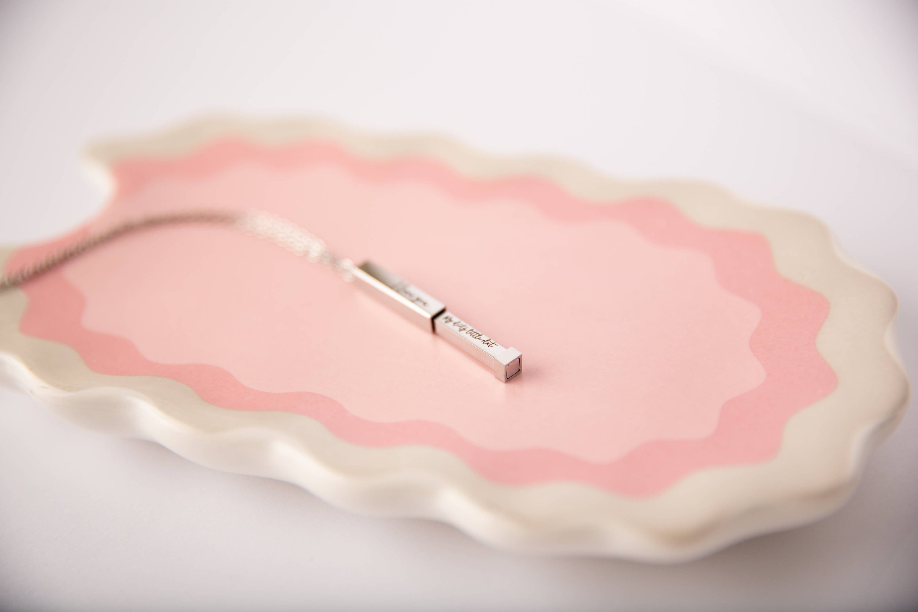Pink and white decorative item with a small rectangular object on a light background