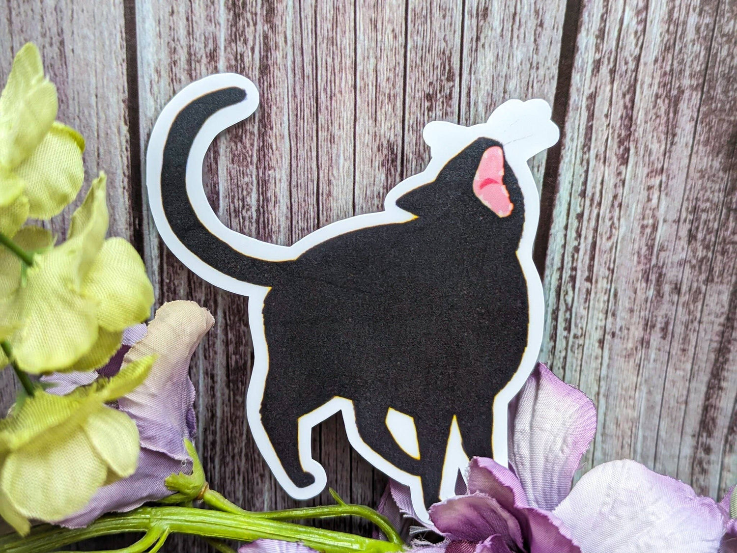 Black cat silhouette with pink nose on a wooden background with flowers