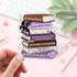 Sticker of stacked books with titles held by a hand on a blurred background