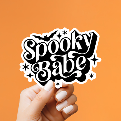 A hand with white manicured nails holds a die-cut sticker that reads &