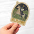 Hand holding a sticker with a unicorn and text on a white background