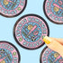 A circular sticker featuring sports romance themes, held by a hand with yellow nail polish against a light blue background with other stickers partially visible.