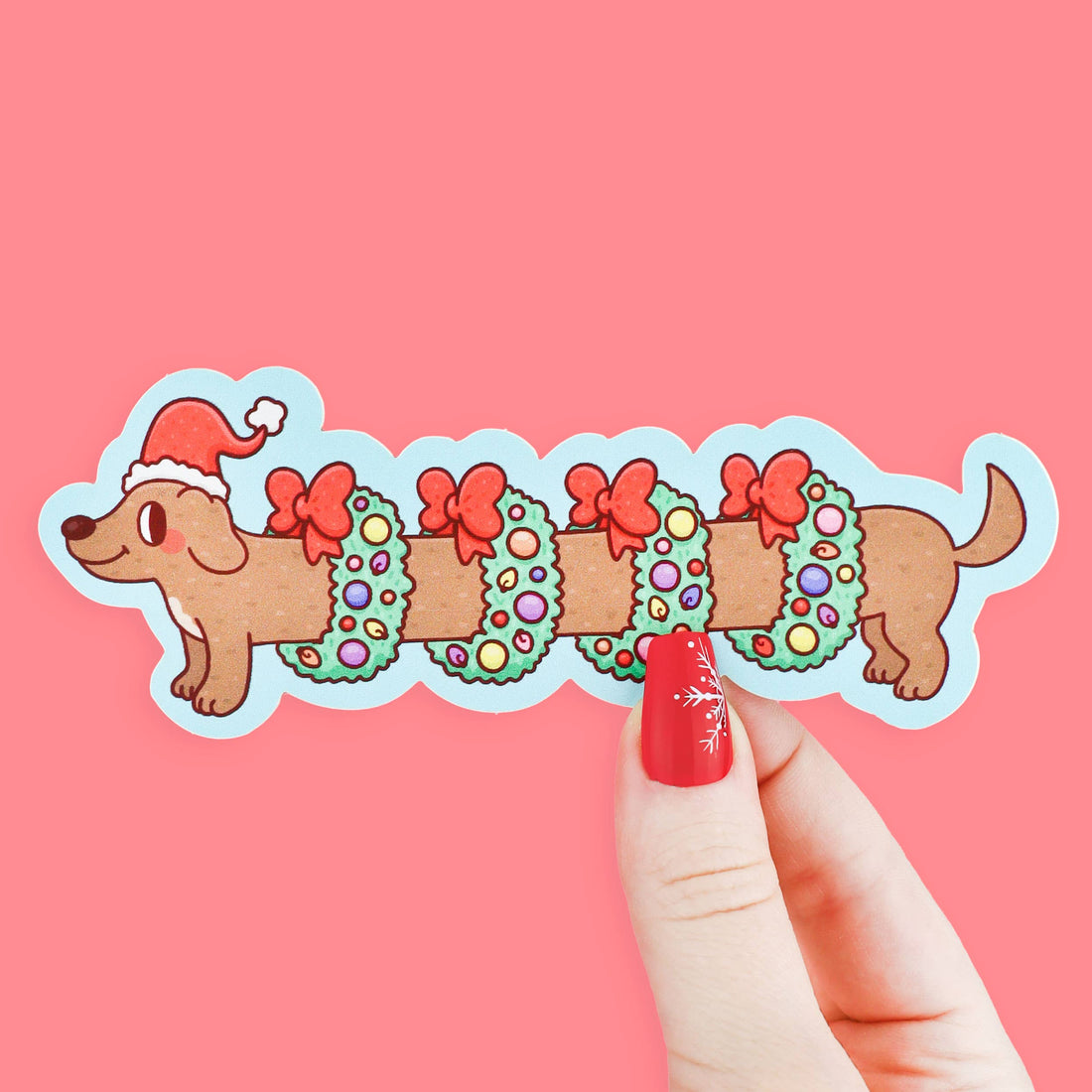 Bookmark of a dog with Christmas decorations held by a hand on a pink background
