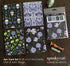 Four floral and nature-themed cards with packaging on a wooden surface, featuring the brand &