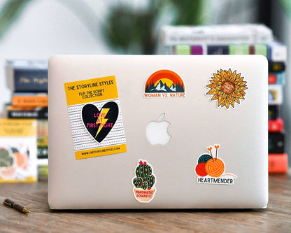 Laptop with various stickers on a wooden surface with books in the background