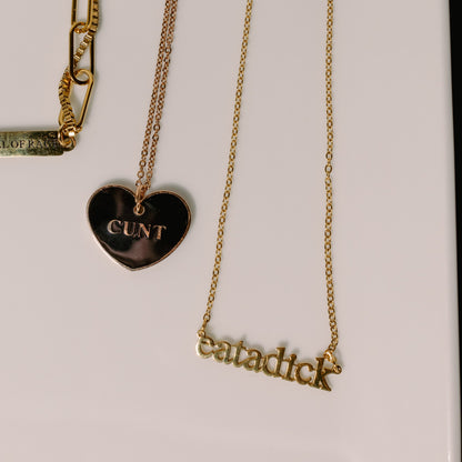 Gold-tone necklaces displayed on a white surface, including a heart-shaped pendant engraved with &