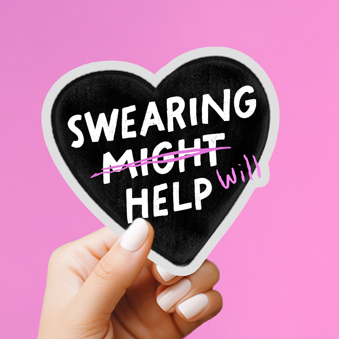 A hand with white manicured nails holds a heart-shaped black sticker or magnet with the phrase &
