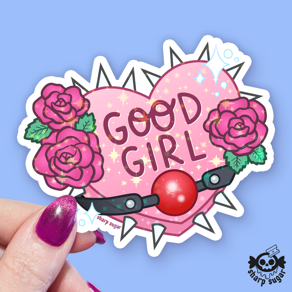 A hand with glittery purple nail polish holds a die-cut sticker featuring a pink heart with the words &