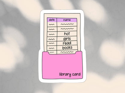A die-cut sticker featuring a pink folder holding a cream-colored library card with a purple header and handwritten-style entries, shown on a soft gray background with blurred light patches.