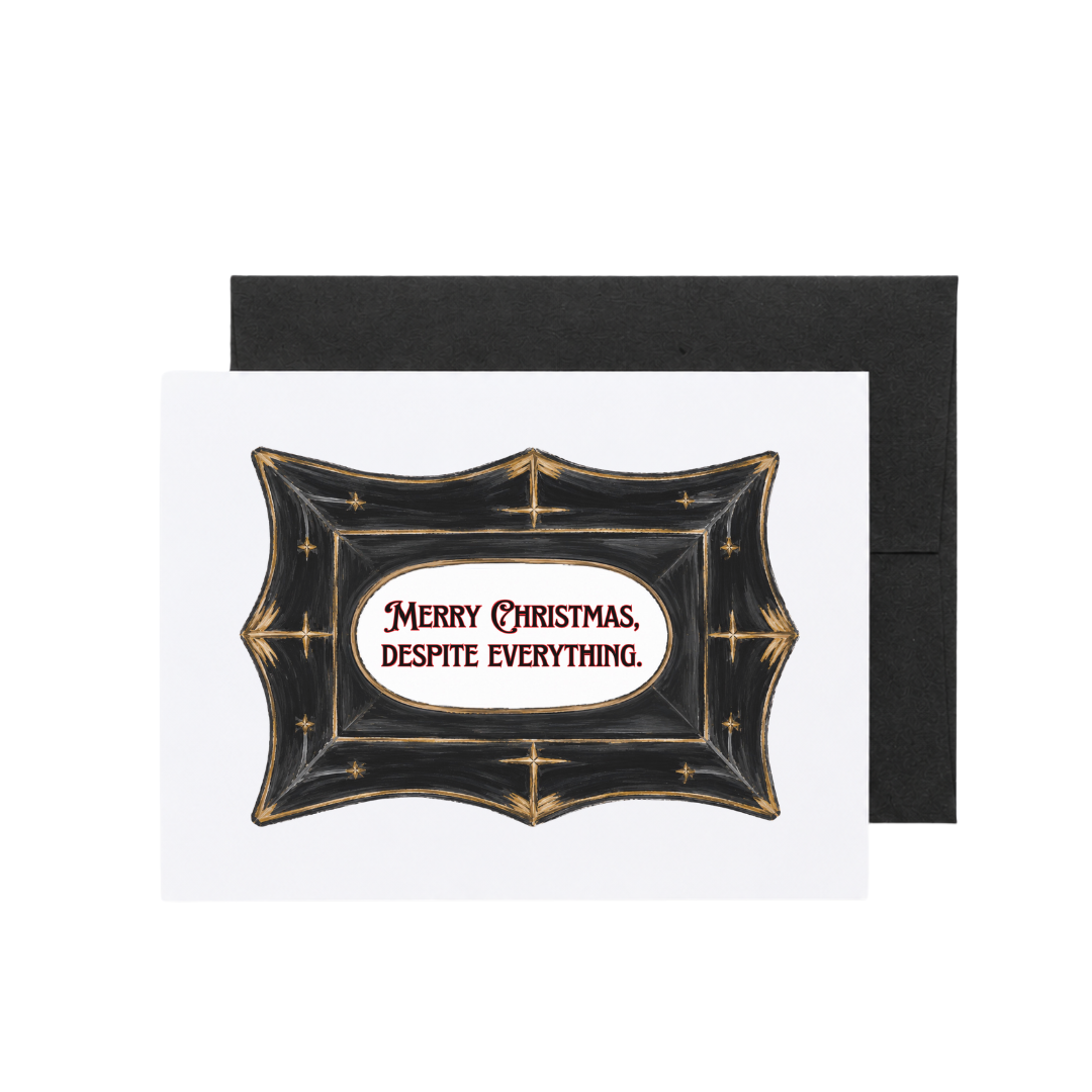 A Christmas greeting card with a black envelope behind it, featuring a decorative black crest with gold stars and the text &