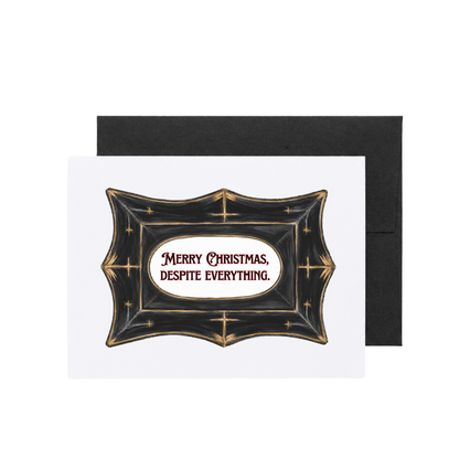A Christmas greeting card with a black envelope behind it, featuring a decorative black crest with gold stars and the text &