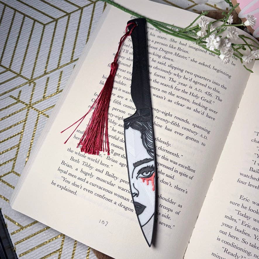Book with a decorative bookmark featuring a face design and red tassel on an open book.