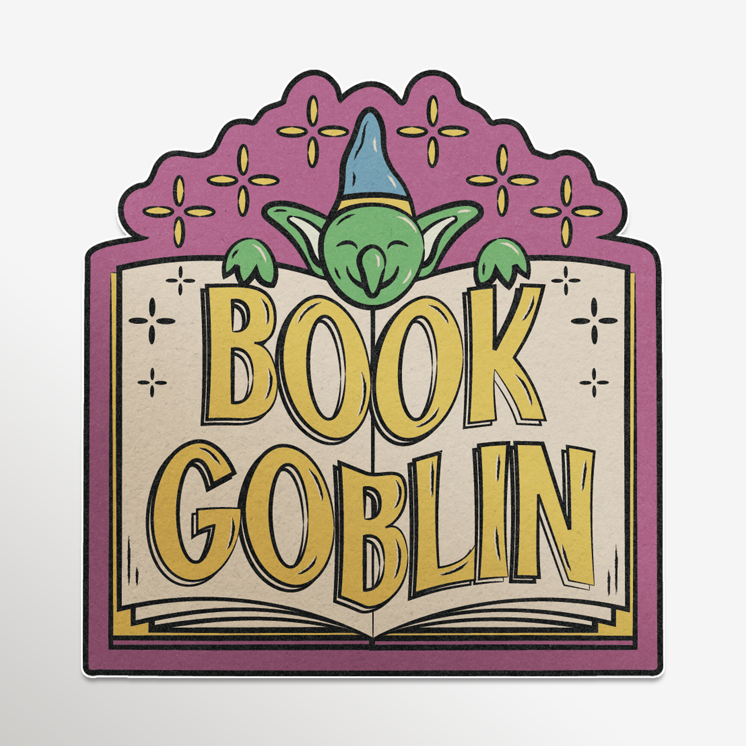 A square decorative graphic or sticker featuring the words “BOOK GOBLIN” in large yellow letters over an open book, with a green goblin face and blue hat peeking above. The design has a purple border and decorative top, shown on a plain light background.