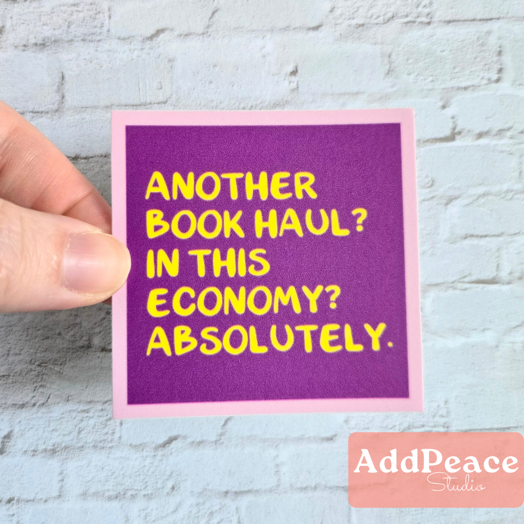 Hand holding a purple card with yellow text on a light gray brick wall background, featuring the brand &