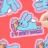 Sticker of a blue bunny reading a book with &
