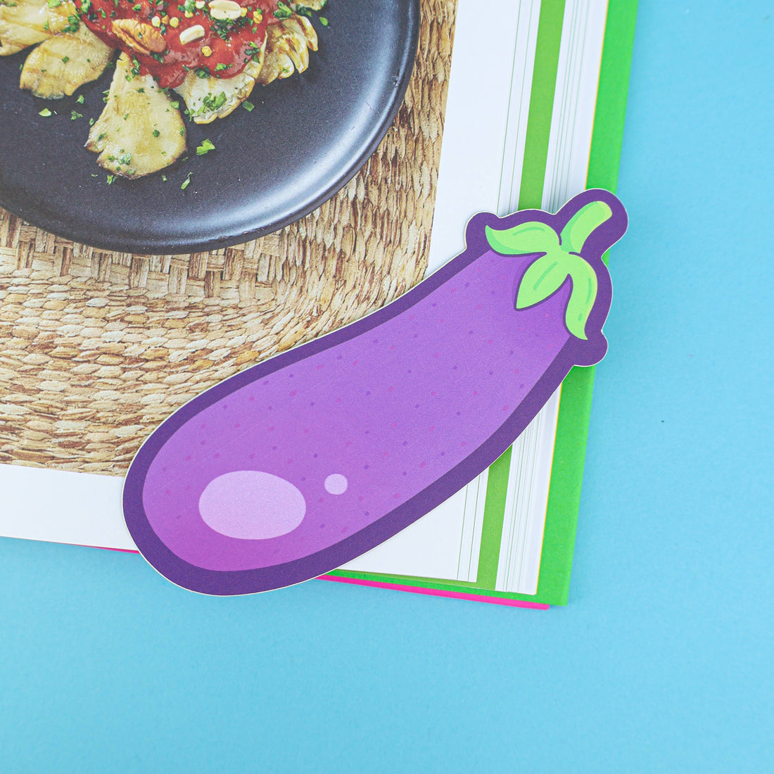 Colorful aubergine-shaped bookmark on a book with a dish in the background
