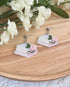 Book-themed earrings with flowers on a wooden surface with white flowers in the background