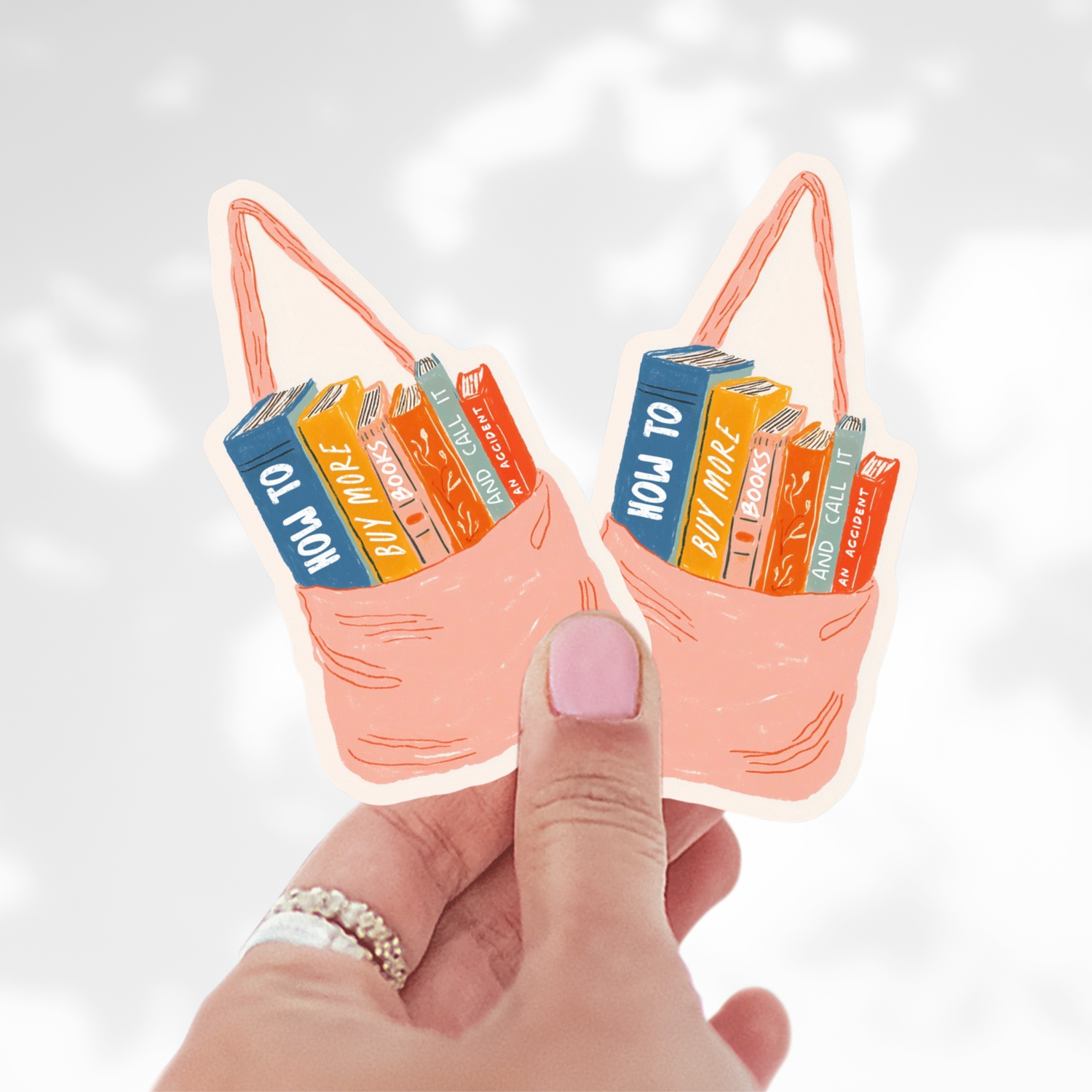 Hand holding two small bags with book designs on a light background