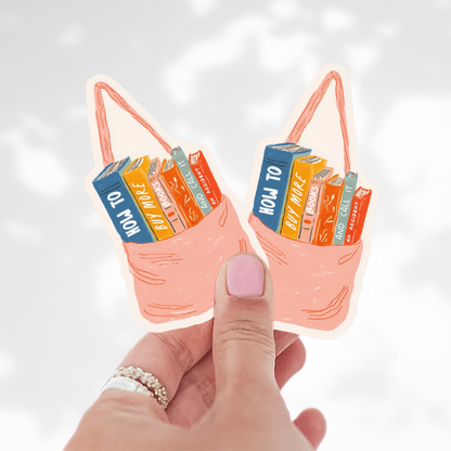 Hand holding two small bags with book designs on a light background