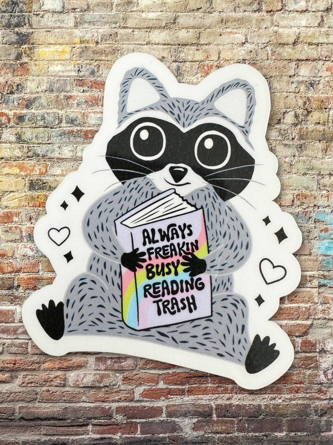Sticker of a raccoon holding a book with text on a brick wall background