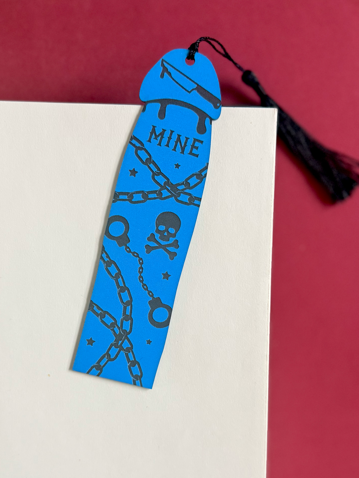 Blue bookmark with black designs on a white book against a red background