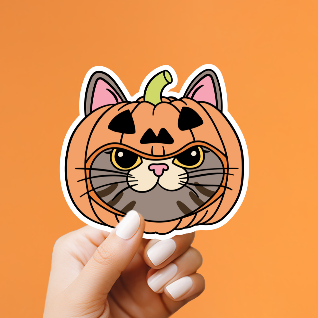 A hand with white manicured nails holds a die-cut sticker shaped like a pumpkin-headed cat face. The sticker features an orange pumpkin body with a green stem, pink inner ears, black triangular eyes and mouth, gray whiskers, and a white border.