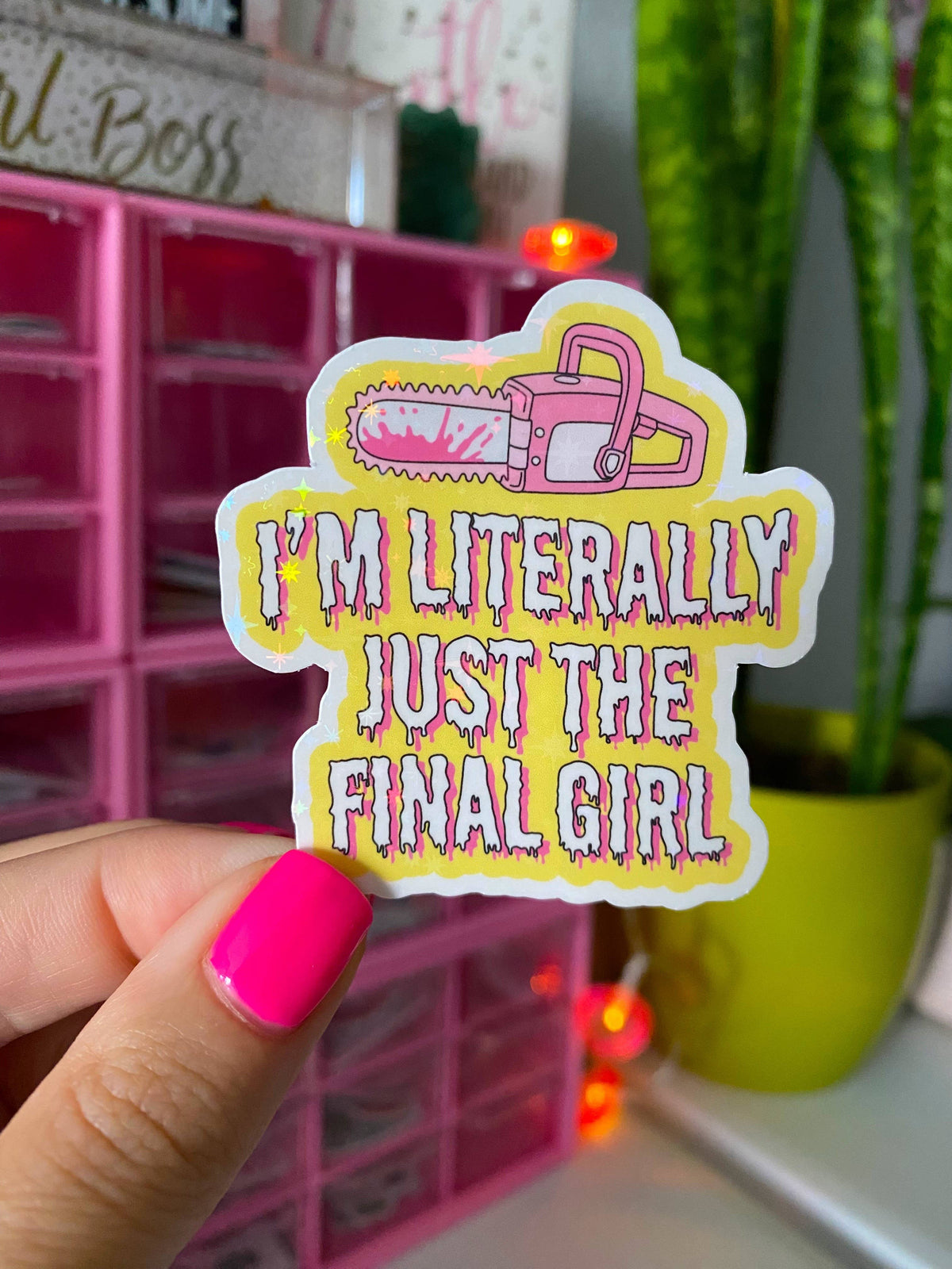 A hand with bright pink nail polish holds a die-cut sticker featuring a pink chainsaw and the text &