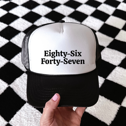 A hand holding a black and white trucker hat with the text &
