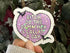 Heart-shaped sticker with text held in front of green leaves