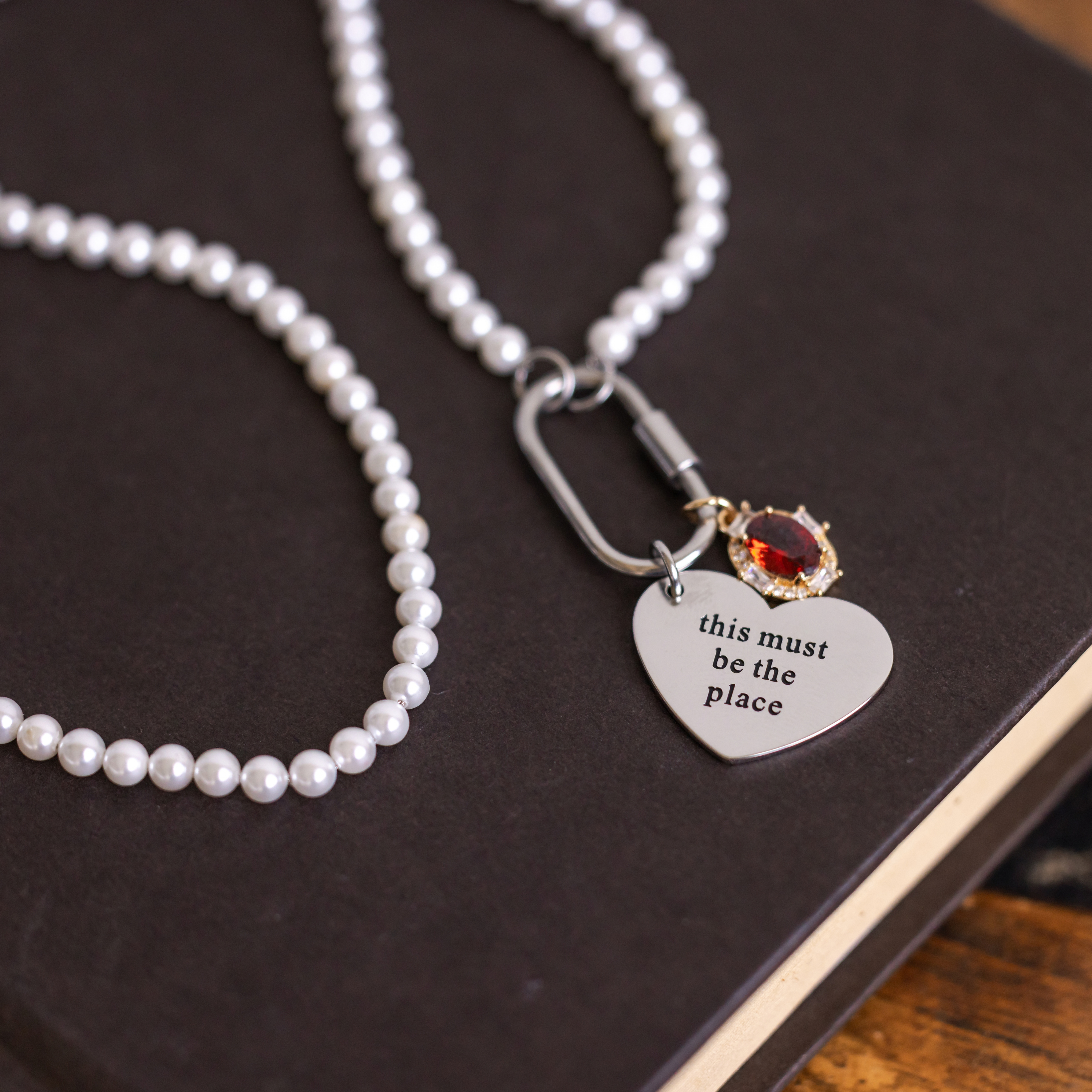 Pearl necklace with a heart-shaped charm and engraved text on a dark surface