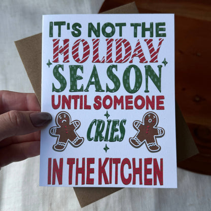 A hand holds a white Christmas greeting card with the text &