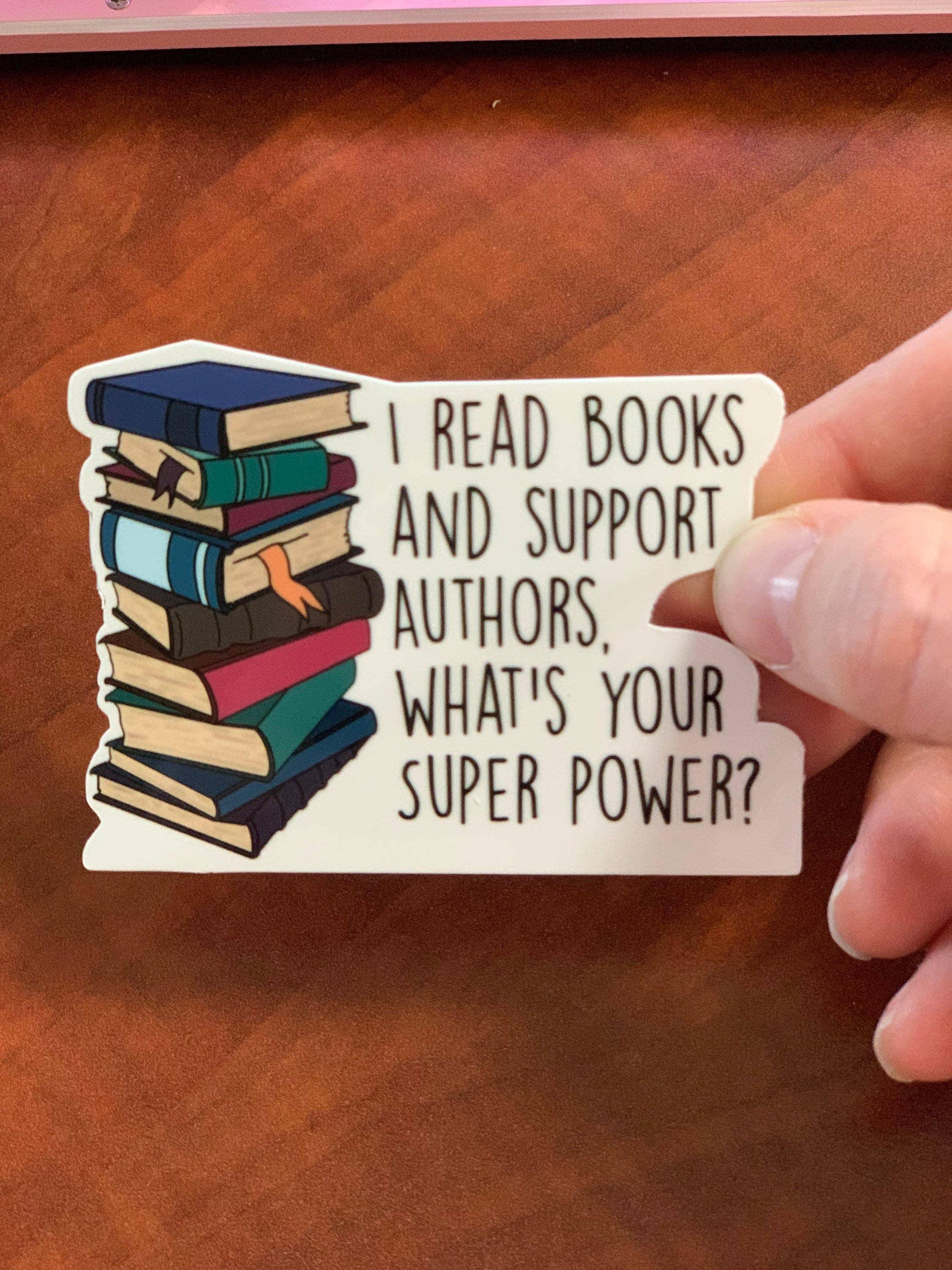 Hand holding a sticker with books and text on a wooden surface