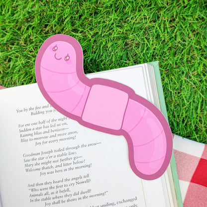 Pink caterpillar-shaped bookmark on an open book with grass in the background