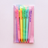 A clear plastic sleeve packaging holds six pastel-colored retractable pens with humorous text printed vertically on them, set against a light pink background.