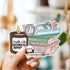 Sticker with book and candle design held by a hand against a blurred background