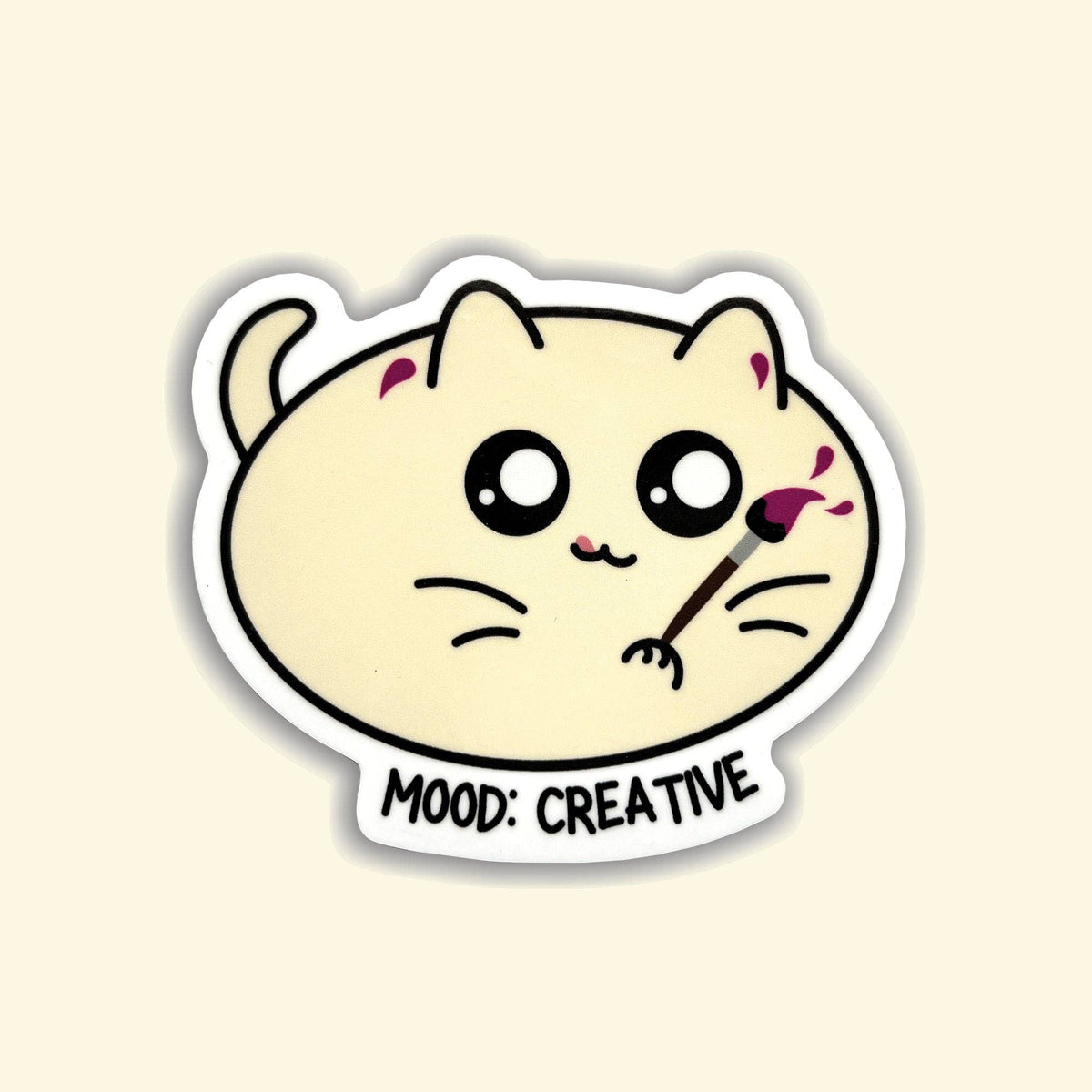 A die-cut sticker featuring a cute cream-colored cartoon cat with large black eyes, holding a paintbrush with pink paint, and the text &