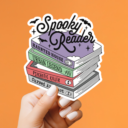 A hand with white manicured nails holds a die-cut sticker featuring a stack of four books with spooky titles and the words &