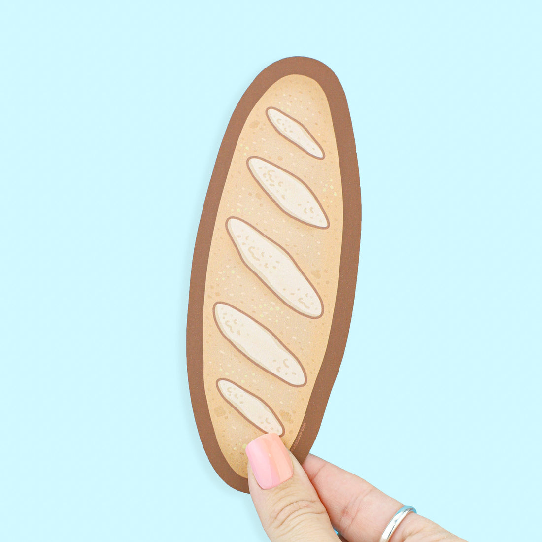 Hand holding a bread-shaped phone case against a light blue background