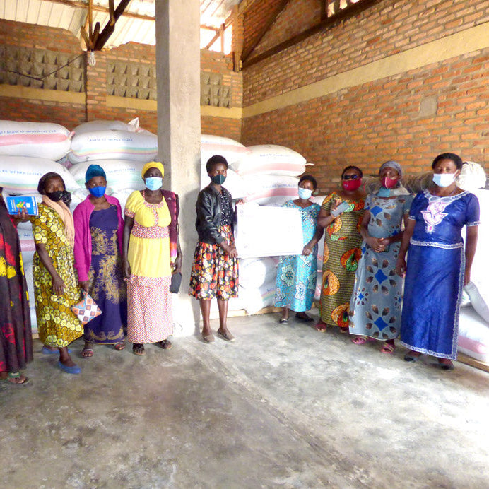 Group of women standing in a warehouse with bags of coffee ready to transport, wearing face masks.