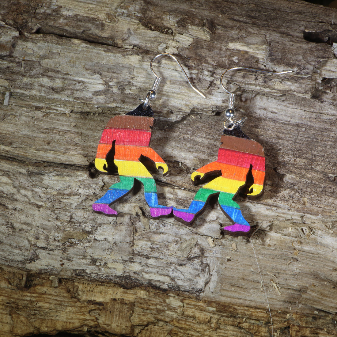 Hand-painted wooden rainbow pride Bigfoot dangle earrings featuring a colorful Sasquatch silhouette with rainbow stripes, hypoallergenic sterling silver hooks, and lightweight LGBTQ+ cryptid jewelry for pride celebrations and Bigfoot fans by Cate&