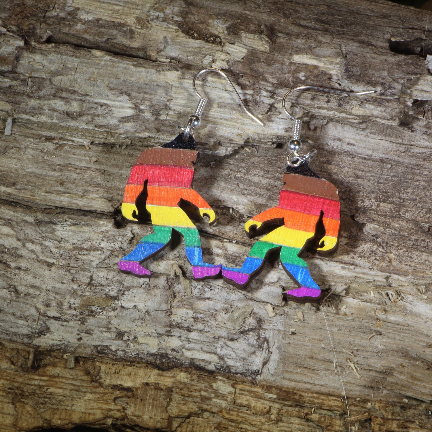 Hand-painted wooden rainbow pride Bigfoot dangle earrings featuring a colorful Sasquatch silhouette with rainbow stripes, hypoallergenic sterling silver hooks, and lightweight LGBTQ+ cryptid jewelry for pride celebrations and Bigfoot fans by Cate&