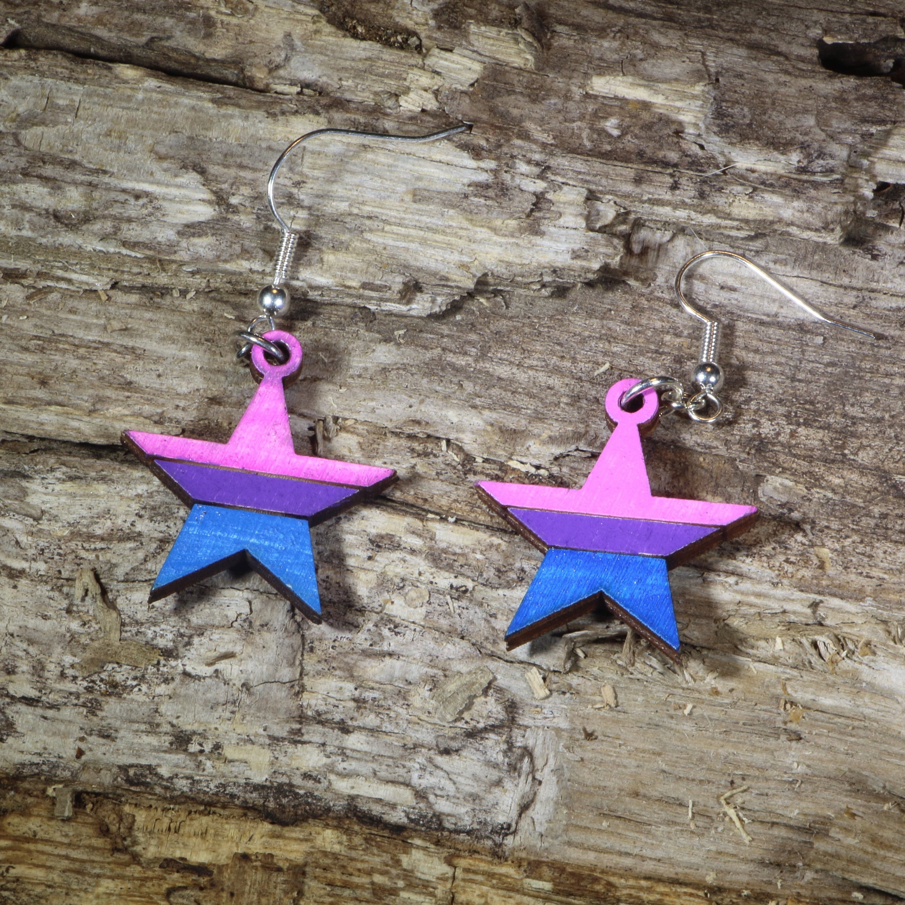 Hand-painted wooden bisexual pride star dangle earrings featuring pink, purple, and blue bisexual flag stripes, hypoallergenic sterling silver hooks, and lightweight LGBTQ+ pride jewelry for bisexual pride celebrations and queer accessory lovers by Cate&