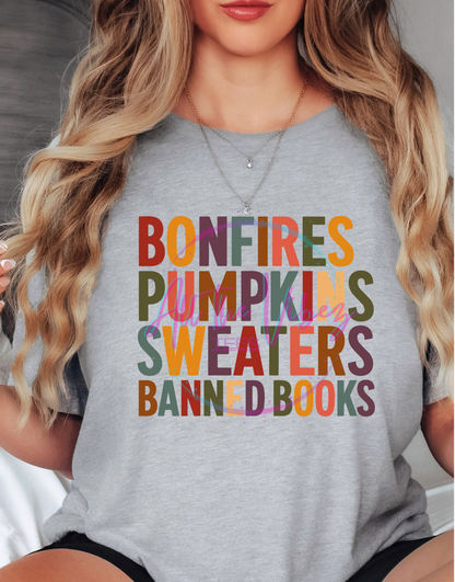Woman wearing Bonfires, Pumpkins, Sweaters &amp; Banned Books fall graphic tee with colorful autumn lettering celebrating cozy season and the freedom to read.