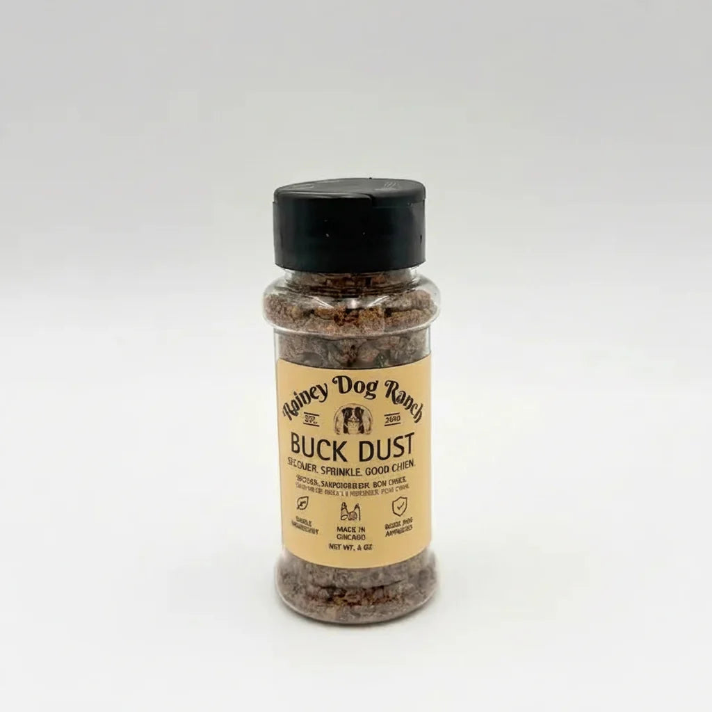 A bottle of Buck Dust dog topper by Rainey Dog Ranch, featuring a tan label and a black cap, set against a plain light gray background.