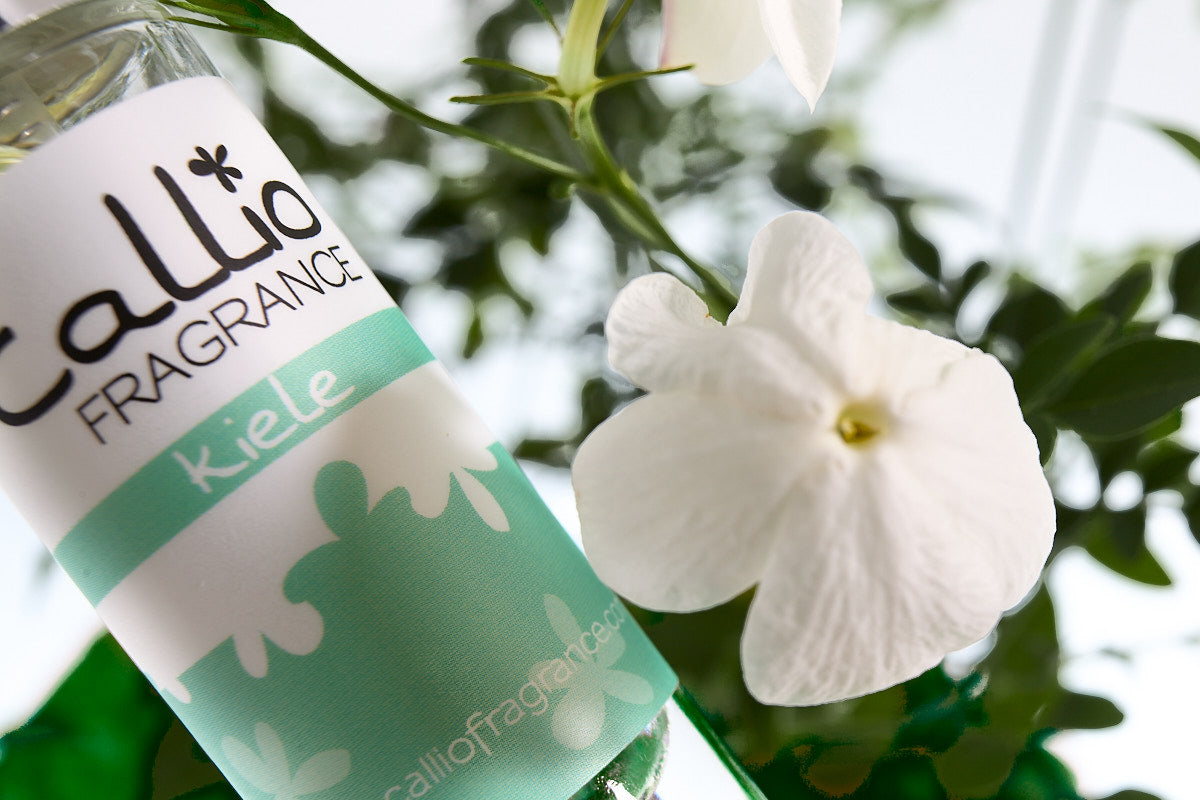Image of a one-ounce bottle of Kiele Travel-Size Perfume, featuring notes of jasmine, gardenia, and tuberose, with jasmine flowers next to it.