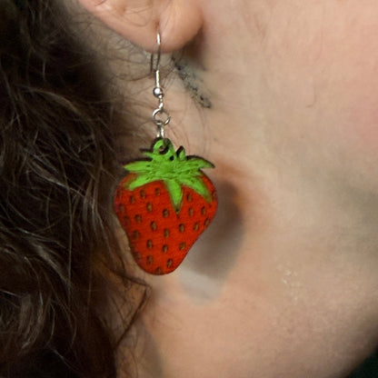 Close-up of a hand-painted wooden strawberry dangle earring featuring a realistic red strawberry with detailed seeds and bright green leaves. This detailed view showcases the handcrafted artwork and lightweight design with a hypoallergenic .925 sterling silver hook, perfect for fruit lovers, gardeners, summer accessories, and everyday statement jewelry.