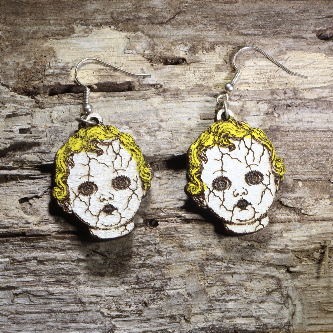 Handcrafted creepy cracked doll head wooden dangle earrings featuring vintage porcelain-style doll faces with cracked details and eerie expressions. Lightweight laser-cut wooden earrings with hypoallergenic .925 sterling silver hooks, perfect for Halloween lovers, horror fans, haunted house actors, gothic fashion, creepy doll collectors, and spooky statement jewelry.