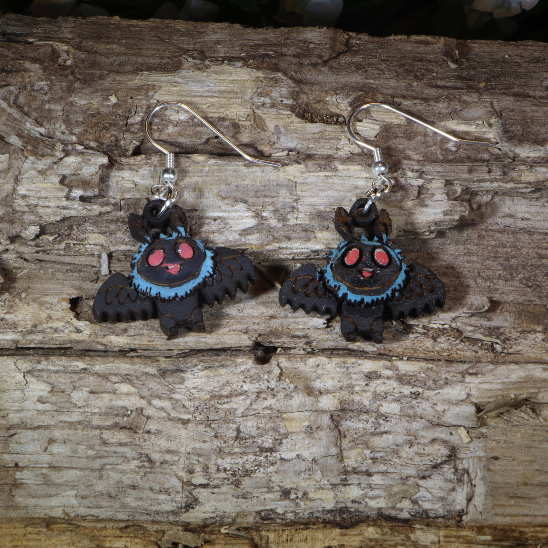 Hand-painted wooden cute Mothman dangle earrings featuring an adorable winged cryptid with glowing red eyes, hypoallergenic sterling silver hooks, and lightweight cryptid mythology jewelry for folklore fans and paranormal enthusiasts by Cate&