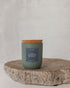 Cypress & Sage Candle in a sage green glass jar with cork lid on a wooden surface against a light gray background
